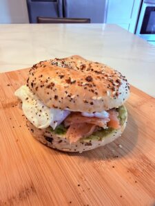 Lox 'n' Loaded Bagel featuring smoked salmon, mashed avocado, red onion, and an over-medium egg on a toasted everything bagel.